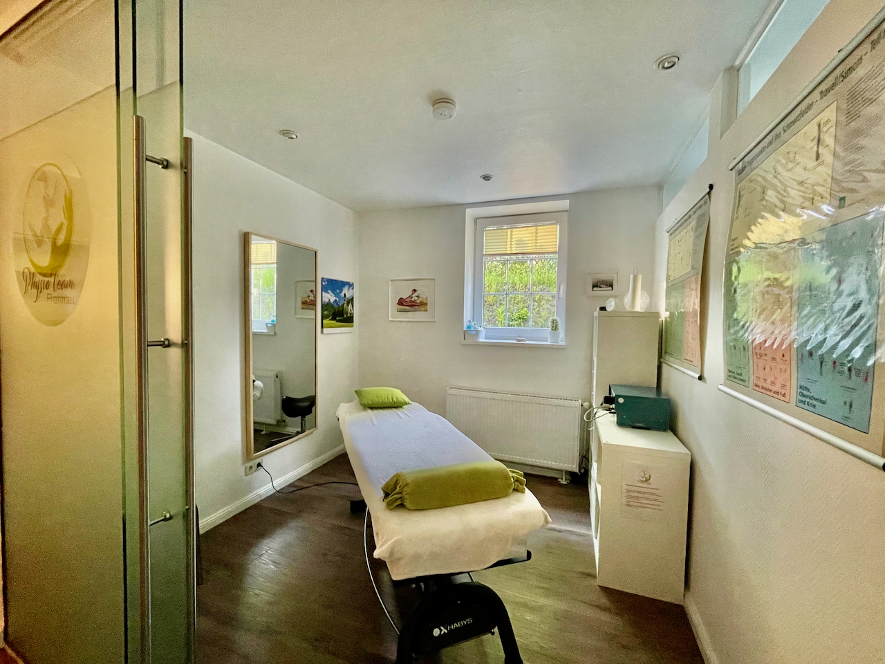 Behandlungsraum mit Therapieliege, Spiegel und Anatomiepostern
